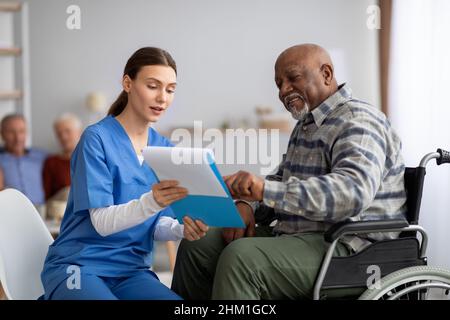 Attraktive junge Krankenschwester hilft älteren schwarzen Mann mit Fragebogen Stockfoto