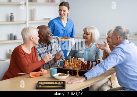 Freundliche Krankenschwester hält Teller mit Cupcakes und spricht mit älteren Menschen Stockfoto