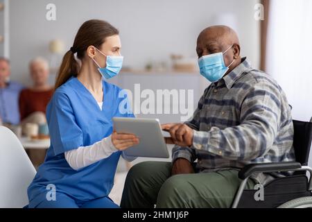 Krankenschwester hilft schwarzen älteren Mann mit digitalen Tablet Stockfoto
