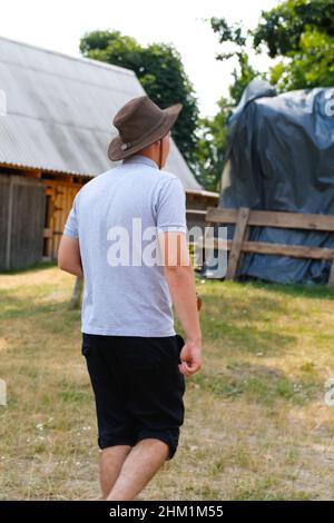 Rüde im Hut. Porträt eines lächelnden Bauern mit grünem Gras und Bäumen Natur im Hintergrund. Junger Mann mit Cowboyhut auf dem Feld. Nahaufnahme. Frohes junges p Stockfoto