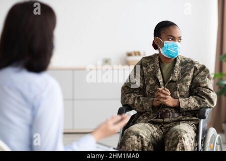 Depressive schwarze Militärfrau im Rollstuhl mit Therapiesitzung mit Psychologin Stockfoto