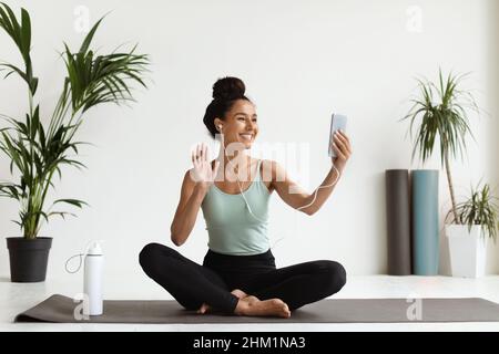 Lächelnde junge Frau mit Smartphone macht Videoanruf mit Yoga-Couch Stockfoto