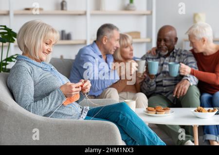 Entspannte ältere Dame beim Stricken, sitzend bei ihren multirassischen Freunden Stockfoto