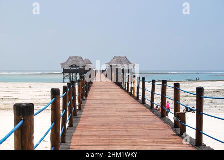 Hölzerner Pier und Strohdächer an einem tropischen Strand, Insel Sansibar. Stockfoto