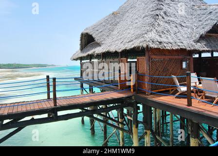 Hölzerner Pier und Strohdächer an einem tropischen Strand, Insel Sansibar. Stockfoto