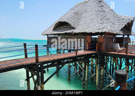 Hölzerner Pier und Strohdächer an einem tropischen Strand, Insel Sansibar. Stockfoto