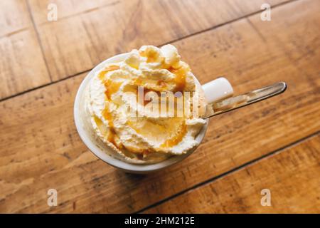 Kaltes Kaffeegetränk Frappe (frappuccino), mit Schlagsahne und Karamellsirup, mit Löffel auf einem Holztisch Stockfoto