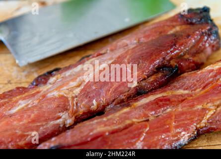 Nahaufnahme ganzer Stücke chinesischen Honiggebratenes Schweinefleisch auf einem Holzbrett, das zum Servieren geschnitten werden kann. Stockfoto