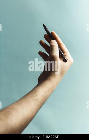 Eine junge Hand schnappte sich einen mechanischen Bleistift auf einem pastellblauen Hintergrund mit tiefen Schatten Stockfoto