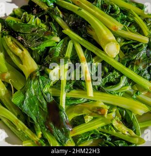 Nahaufnahme eines Tellers mit frischem Kai Lan, einem chinesischen Gemüse, serviert mit einem Spritzer Sesamöl und Austernsauce. Stockfoto