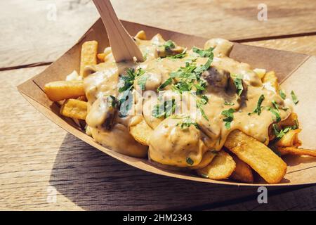 pommes Frites mit Pilzsauce und Käse in einer Papierschüssel mit auf einem Holztisch Stockfoto