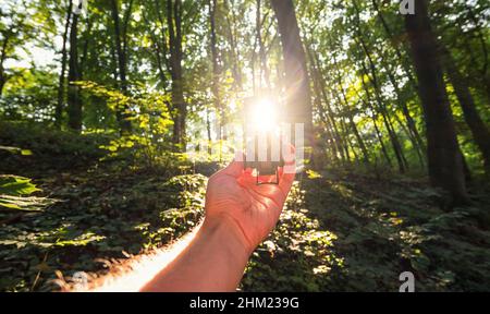 Reisender Mann sucht Richtung mit einem Kompass in den tiefen Wäldern. Blickpunkt aufgenommen mit explosivem Sonnenlicht Stockfoto