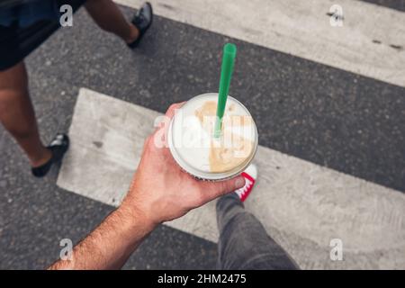 Junger Mann, der auf Zebrastreifen in der Stadt mit Kaffee geht, um in der Hand zu gehen, aus Sicht der Perspektive. Stockfoto
