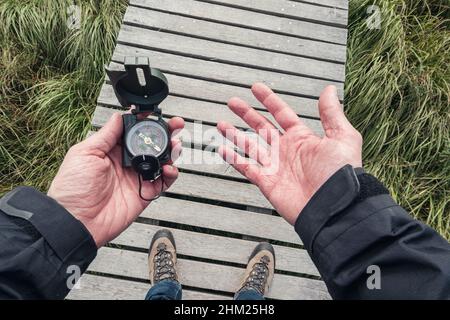 Mann halten einen Kompass und Suche Richtung der Richtung auf einer hölzernen Promenade, Sicht. Stockfoto