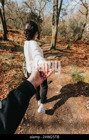 Eine Frau in der Mitte des Waldes hält die Hand des Fotografen mit einem Gummiring beim Gehen Stockfoto