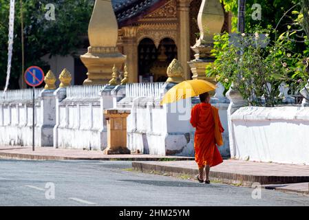 Junger buddhistischer Mönch, der an einem Tempel in Luang Prabang, Laos, vorbeikommt, mit einem Rauchverbotsschild auf der linken Seite Stockfoto