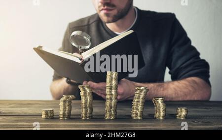 Mann überprüft Finanzen mit Lupe mit Münzen auf Stapeln Stockfoto