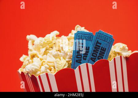 Popcorn in gestreifter Schachtel mit zwei Kinokarten auf rotem Hintergrund Stockfoto