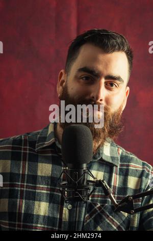 Junger Hipster-Mann in der Nähe eines Streaming-Mikrofons, der mit einem roten Hintergrund lächelt und Platz zum Kopieren hat