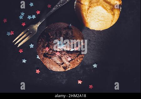 Schokoladenmuffin und Vanillemuffin mit Gabel, hausgemachte Bäckerei, auf dunklem Hintergrund Stockfoto