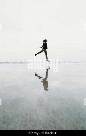 Junge Frau springt am Strand mit einer Reflexion über das Wasser mit Kopie Raum Freiheit Konzept springen Stockfoto