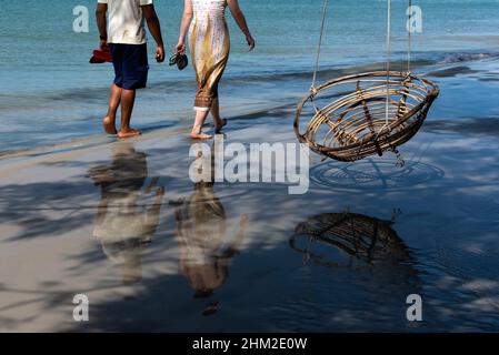 Mann und Frau gehen am Strand mit Schaukel auf der rechten Seite Stockfoto