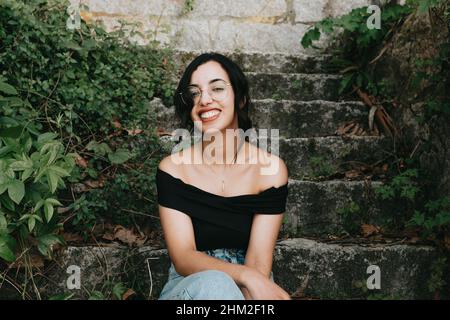 Junge schöne afrikanische Frau lächelt vor der Kamera auf Federkleidung und Brille Stockfoto