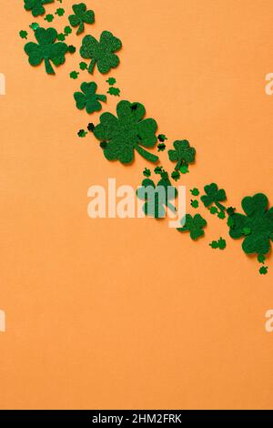 Happy St. Patrick's Day Komposition. Grüne Kleeblätter auf orangefarbenem Hintergrund. Flach liegend, Draufsicht. Stockfoto