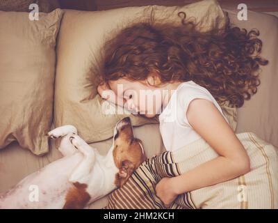 Süßes lockiges Mädchen und Jack russell Hund schläft in der Nacht. Stockfoto