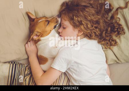 Süßes lockiges Mädchen und Jack russell Hund schläft in der Nacht. Stockfoto