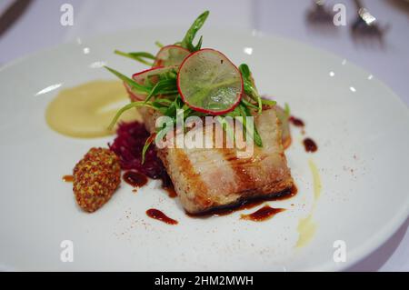 In Scheiben geschnittener knusprig gebratener Schweinebauch mit Sauce auf weißem Teller im asia Fusion Dish Restaurant Stockfoto