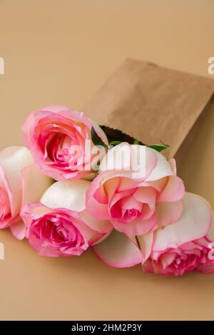 Zarte rosafarbene Rosen in einer Bastelpapiertasche auf beigem Hintergrund. Minimalistisch trendige Komposition. Abstrakte Kunstidee. Romantische rosa Rosenblüten in Pastelltönen. Moderne Ästhetik. Neutrale Erdtöne. Grußkarte Hintergrund Kopierbereich Banner Stockfoto