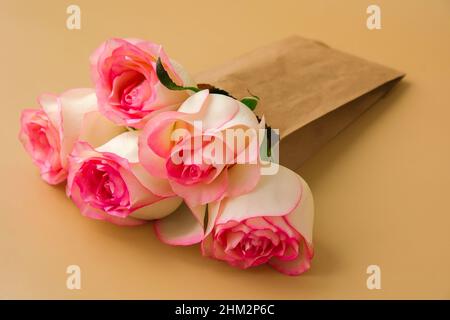 Zarte rosafarbene Rosen in einer Bastelpapiertasche auf beigem Hintergrund. Minimalistisch trendige Komposition. Abstrakte Kunstidee. Romantische rosa Rosenblüten in Pastelltönen. Moderne Ästhetik. Neutrale Erdtöne. Grußkarte Hintergrund Kopierbereich Banner Stockfoto