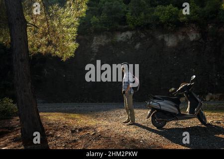 Junge Frau im Motorradhelm stehen neben Roller auf der Asphaltstraße. Stockfoto