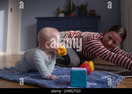 Mutter mit Baby macht Yoga zu Hause, um stark und gesund zu sein Stockfoto