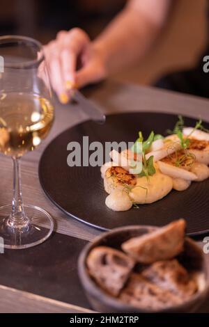 Gegrillte Hokkaido-Jakobsmuscheln, Pastinaip-Püree, Yuzu- und Birnenwürze, serviert mit einem Weinglas Stockfoto