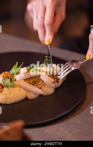 Gegrillte Hokkaido-Jakobsmuscheln, Pastinaip-Püree, Yuzu- und Birnenwürze, serviert mit einem Weinglas Stockfoto