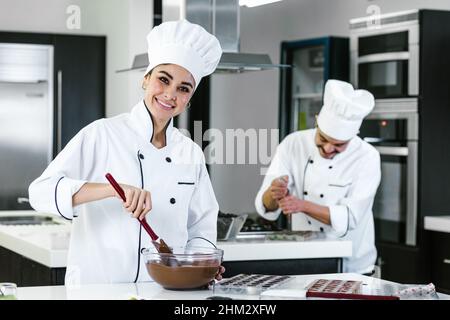 lateinamerikanische Konditorin in Uniform mit einer Schüssel, die köstliche Süßigkeiten und Pralinen in der Küche in Mexiko, Lateinamerika, zubereitet Stockfoto