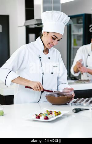 lateinamerikanische Konditorin in Uniform mit einer Schüssel, die köstliche Süßigkeiten und Pralinen in der Küche in Mexiko, Lateinamerika, zubereitet Stockfoto