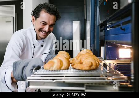 Junger lateinischer Bäcker und Backen von Croissant und Brot im Ofen in der Küche in Mexiko Lateinamerika Stockfoto