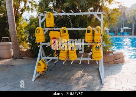 Stapel von hängenden gelben Rettungswesten auf Kleiderbügeln draußen während der Marine-Aktivitäten, Sicherheitskleidung, Schutzkonzept. Stockfoto