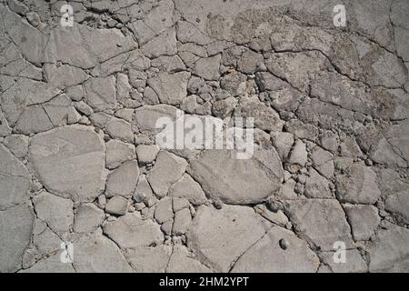 Grauer Betonboden, der in einen zufällig großen Gesteinshintergrund gesprungen ist Stockfoto