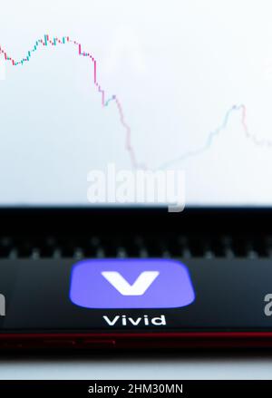 Rottweil, Deutschland. 06th. Februar 2022. Das Logo von Vivid ist auf dem Display eines iPhone zu sehen, während auf einem Monitor im Hintergrund ein Candlestick-Chart einer Kryptowährung zu sehen ist. Die Berliner Smartphone-Bank Vivid nähert sich nach einer Finanzierungsrunde einer Milliardenbewertung. Kunden können ihr Geld auch in Aktien, Fonds, Kryptowährungen und andere Finanzprodukte in der Vivid App investieren. Kredit: Silas Stein/dpa/Alamy Live Nachrichten Stockfoto