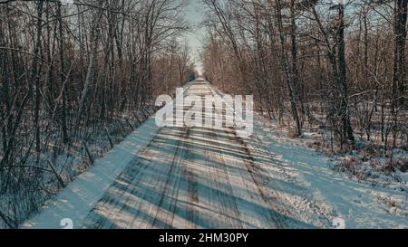 Unbefestigte Straße mit Schnee bedeckt, während die Sonne durch die Bäume scheint. Stockfoto