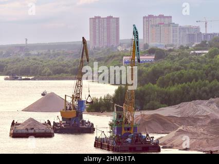 Nowosibirsk, Sibirien, Russland-10.10.2019: Schwimmkrane auf der Bank des ob. Schwimmende Krane entladen Lastkähne nahe der Küste. Mehrstöckige Häuser und Stockfoto