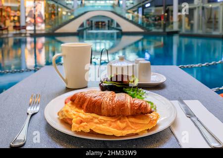 Tasse Kaffee mit einem Croissant und Ei-Sandwich zum Frühstück in einem Café in einem luxuriösen Einkaufszentrum mit hochwertigen Restaurants und Geschäften in Singapur Stockfoto