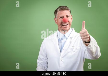 Wissenschaftler mit weißem Mantel hat rote Clownnase auf und steht vor grünem Hintergrund Stockfoto
