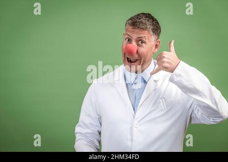 Wissenschaftler mit weißem Mantel hat rote Clownnase auf und steht vor grünem Hintergrund Stockfoto