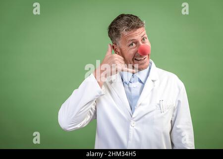 Wissenschaftler mit weißem Mantel hat rote Clownnase auf und steht vor grünem Hintergrund Stockfoto