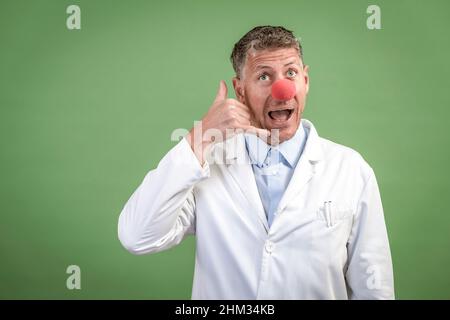 Wissenschaftler mit weißem Mantel hat rote Clownnase auf und steht vor grünem Hintergrund Stockfoto